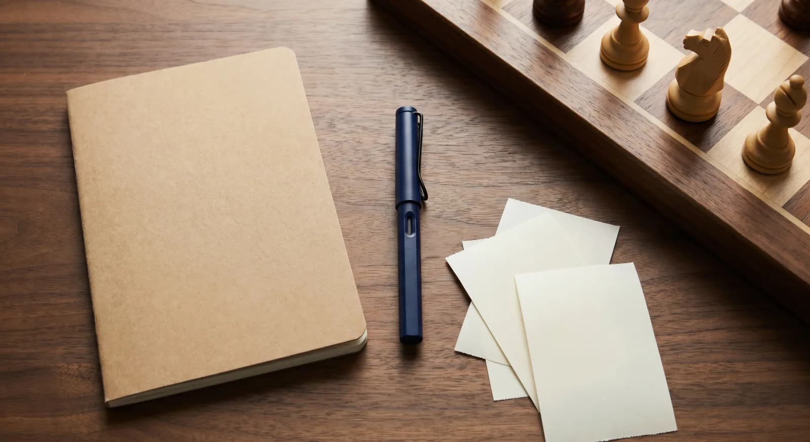 A paper class register, fountain pen, and blank receipt slips next to a wooden chessboard on a desk